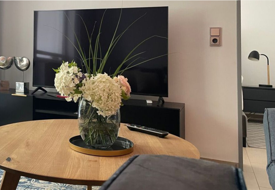 Wohnraum mit TV und Tisch mit Blumen darauf
